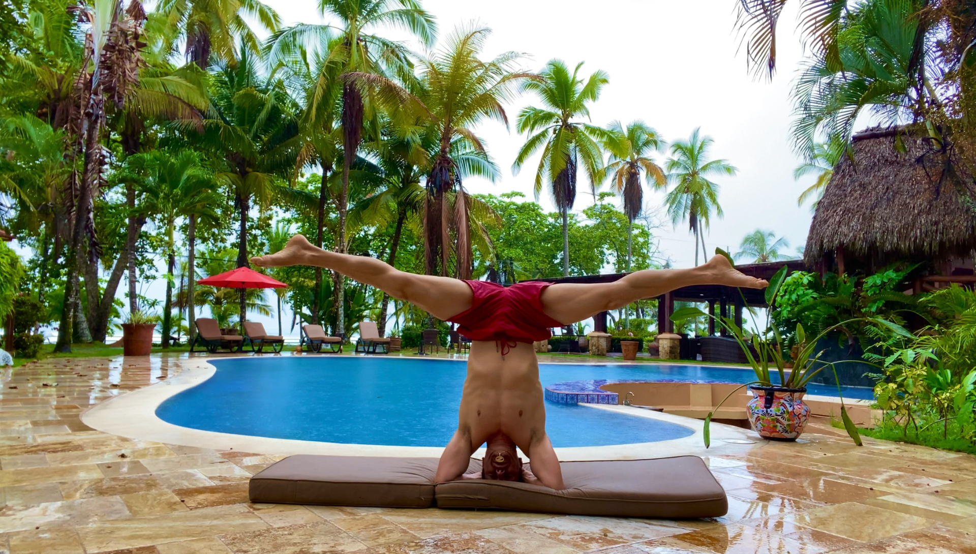 Headstand split among palm trees by a tropical pool
